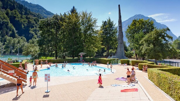 A swimming pool surrounded by a park with a mountain backdrop. - ALLEMONT Chalet des Galline DOMAINE VAUJANY ALPE D HUEZ  (Allemond)
