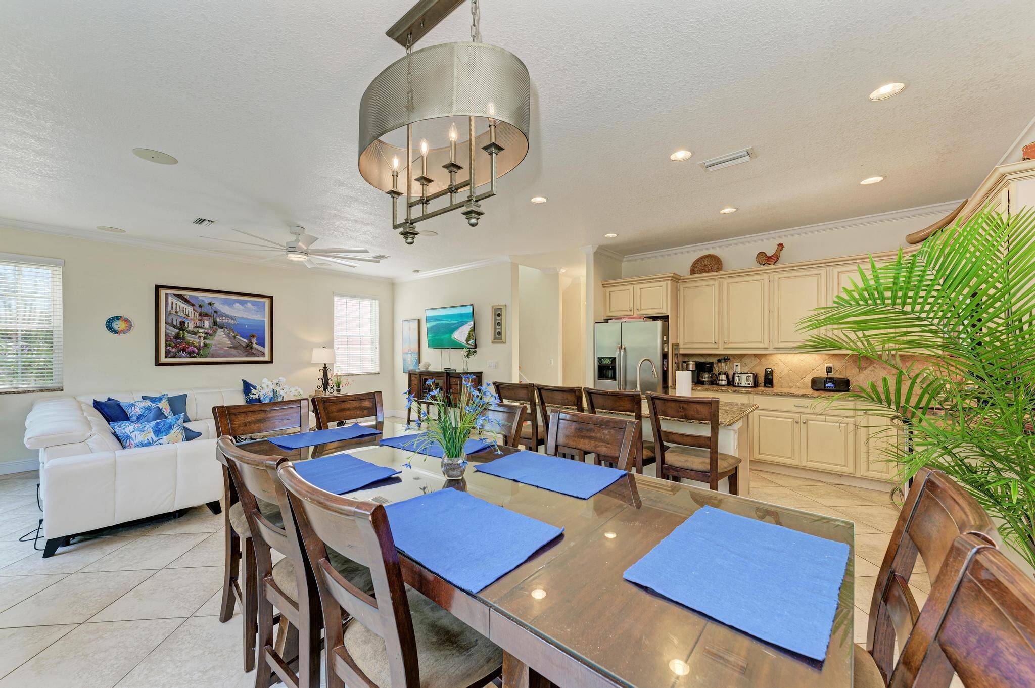 A spacious dining area with a wooden table, blue placemats, and a chandelier.