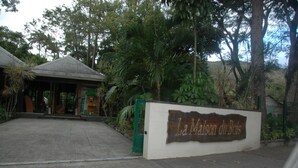 A sign for La Maison du Bois, a building with a covered entrance and surrounded by lush greenery. - Bungalows with swimming pool with breathtaking sea and mountain views for 4 people each (BOUILLANTE)