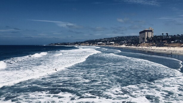 A beach with waves, a building, and a clear sky. - Ocean View Beach House On Jersey Ct just steps to the beach (San Diego)