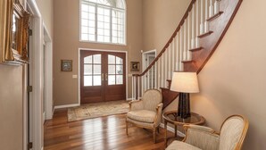 A spacious foyer with a wooden staircase, a large arched window, and a traditional chair. - 6BR Alexandria Lakefront, FREE Pontoon, Designed for Groups (Alexandria)