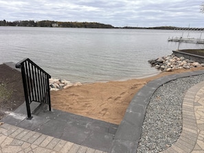 A lakeside walkway with a bench, a sandy area, and a dock.