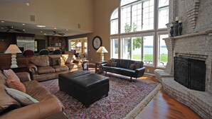 A spacious living room with leather sofas, a fireplace, and large windows overlooking a scenic view. - 6BR Alexandria Lakefront, FREE Pontoon, Designed for Groups (Alexandria)