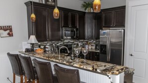 A modern kitchen with dark wood cabinets, a stainless steel refrigerator, and a marble island with bar stools. - Spacious Home. Short Walk to Beach, Beach Shuttle & Shunk Gulley. Pet Friendly! (Santa Rosa Beach)