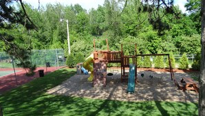 Une aire de jeux avec un toboggan, des balançoires et une structure d’escalade, le tout entouré d’arbres.