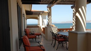 A covered outdoor seating area with chairs and a table, overlooking a body of water. - Beachfront  Luxury Penthouse at Paraiso Del Mar (La Paz)