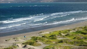 A coastal landscape with a beach, ocean waves, and distant mountains. - Beachfront  Luxury Penthouse at Paraiso Del Mar (La Paz)