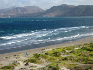 A coastal landscape with a beach, ocean waves, and distant mountains. - Beachfront Luxury Penthouse at Paraiso Del Mar (La Paz)