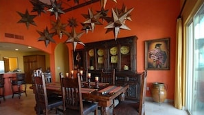 A dining area with a wooden table and chairs, a decorative ceiling with star-shaped elements, a cabinet with glass doors, and a painting on the wall. - Beachfront  Luxury Penthouse at Paraiso Del Mar (La Paz)