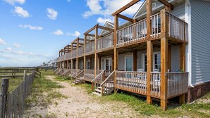 Een hotel aan het strand met houten balkons, een zandpad en een houten hek.