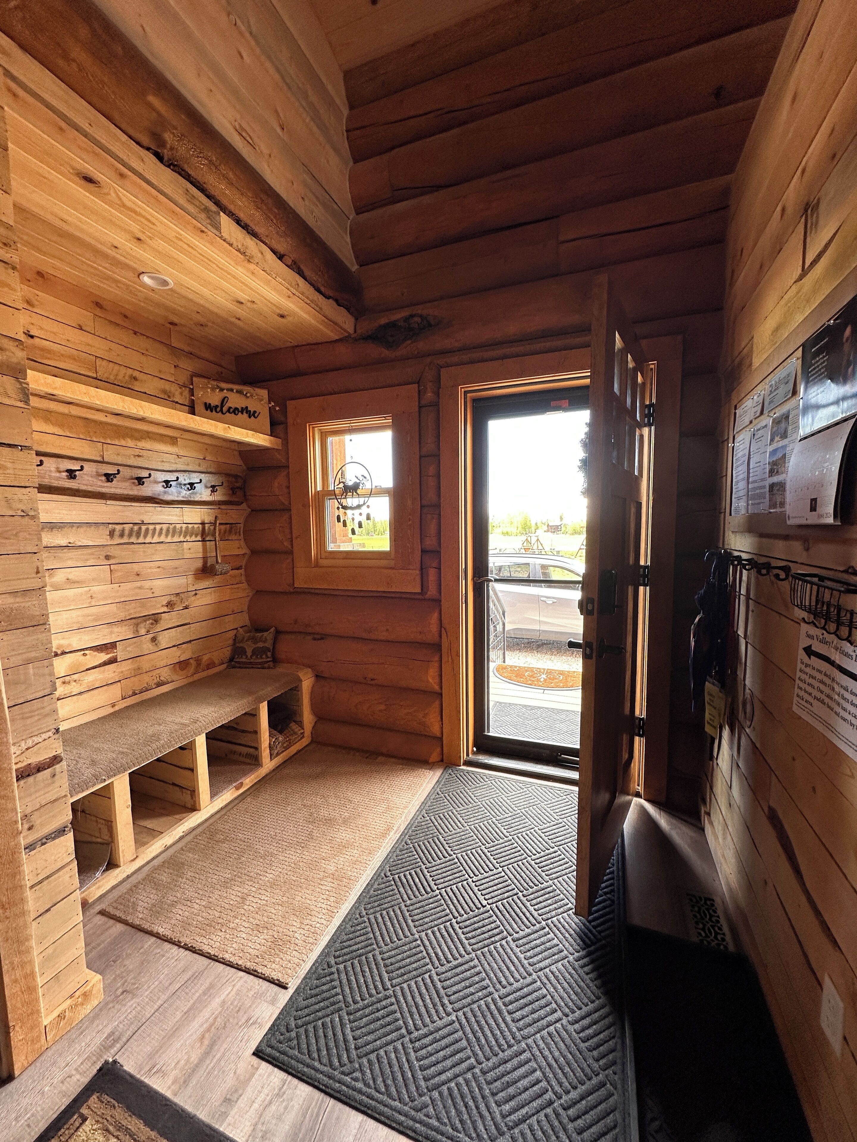 A wooden cabin interior with a bench, a small window, and a door leading outside.