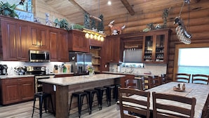 A spacious kitchen with wooden cabinets, a large island, bar stools, and a dining area with wooden chairs. - Dates open -See Fall Colors-Christmas-Winter Fun-Perfect Family Gathering Cabin! (Grand Lake)