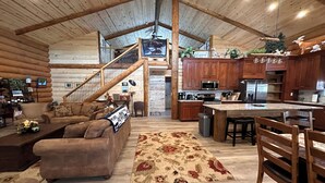 Interior espaçoso de uma cabana de madeira, com sala de estar, cozinha e escada para um andar superior.