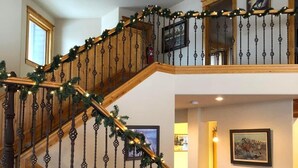 A staircase with a wooden railing and garland, a leather sofa, a lamp, and a painting on the wall.
