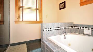 Ein Badezimmer mit Badewanne, Fenster mit Jalousien und einer gefliesten Rückwand.