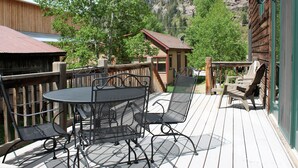 A wooden deck with a metal table and chairs, overlooking a mountainous landscape.