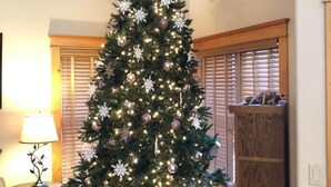 A Christmas tree with lights and ornaments in a room with wooden blinds and a lamp.