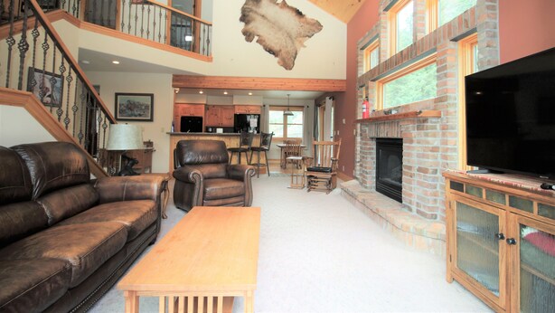 A spacious living area with a fireplace, leather sofa, wooden table, and a mounted animal hide on the ceiling.