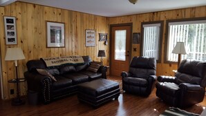 A cozy living room with wooden walls, a leather sofa, a leather armchair, and a coffee table. There are framed pictures on the walls and a sign reading "Rocky Mountain National Park". - 10% Discount to Veterans, First Responders, and Seniors. Note status in request. (Estes Park)