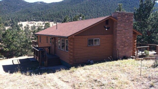 A wooden cabin with a brick chimney, a deck, and a view of a forested mountain. - 10% Discount to Veterans, First Responders, and Seniors. Note status in request. (Estes Park)