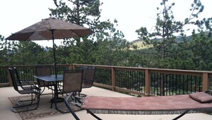 A deck with outdoor furniture, including a table and chairs, and a lounge chair with a cushion. - 10% Discount to Veterans, First Responders, and Seniors. Note status in request. (Estes Park)