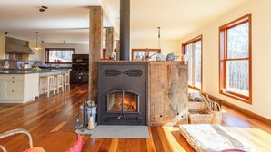 Amplia sala de estar con una estufa de leña central, suelo de madera y ventanas grandes que ofrecen luz natural.