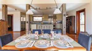 Un comedor con una mesa larga dispuesta para seis personas, una cocina al fondo y vistas al exterior.