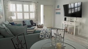 Una sala de estar moderna con una mesa de comedor de vidrio, un sofá y un televisor de pantalla plana montado en la pared.