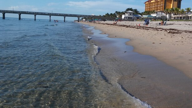 Una playa con agua cristalina, un puente y un edificio grande con techo rojo.