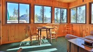 A wooden cabin with large windows, a dining table, chairs, and a sofa. - Excellent reviews. Perfect for ALL ages-families, kids, dogs allowed. Hot tub! (Grand Lake)