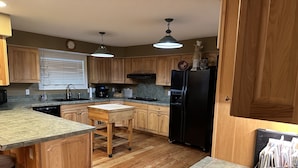 A kitchen with wooden cabinets, a black refrigerator, a wooden island, and a countertop with a coffee maker. - Excellent reviews. Perfect for ALL ages-families, kids, dogs allowed. Hot tub! (Grand Lake)
