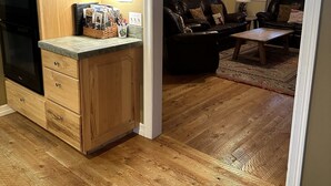 A kitchen with wooden cabinets and a black refrigerator. There is a dining area with a leather couch and a coffee table. - Excellent reviews. Perfect for ALL ages-families, kids, dogs allowed. Hot tub! (Grand Lake)