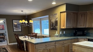 A kitchen with wooden cabinets, a large island, and a dining area with chairs and a table. - Excellent reviews. Perfect for ALL ages-families, kids, dogs allowed. Hot tub! (Grand Lake)