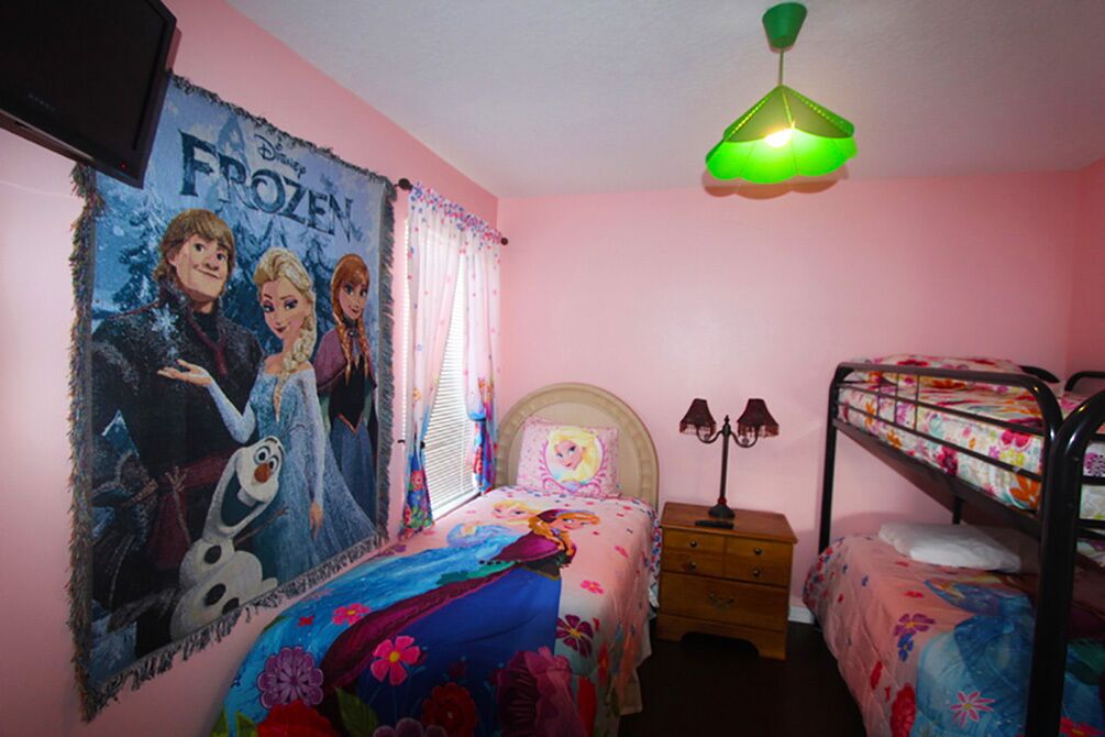 Ein Schlafzimmer mit Bett, Nachttisch, Kommode, Etagenbett, einem Poster mit Figuren aus 'Frozen' und einer hängenden, grünen Leuchte.