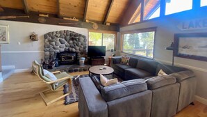 A cozy living room with a stone fireplace, a large gray sectional sofa, a wooden ceiling, and a view of the outdoors. - Fun and Relaxing in Tahoe City! (Tahoe City)