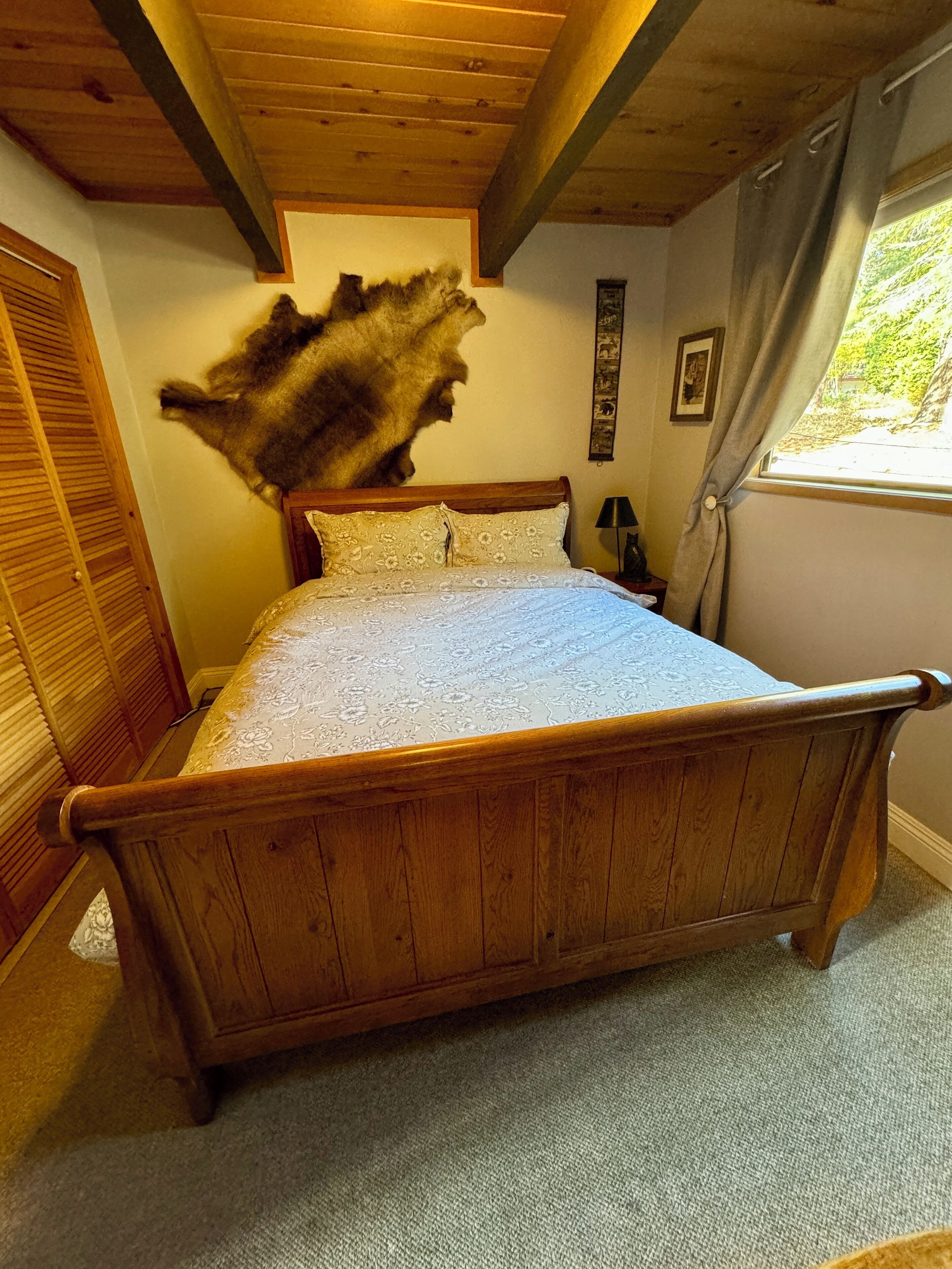 Un letto in legno con copriletto floreale in una stanza con soffitto in legno e finestra con tende.