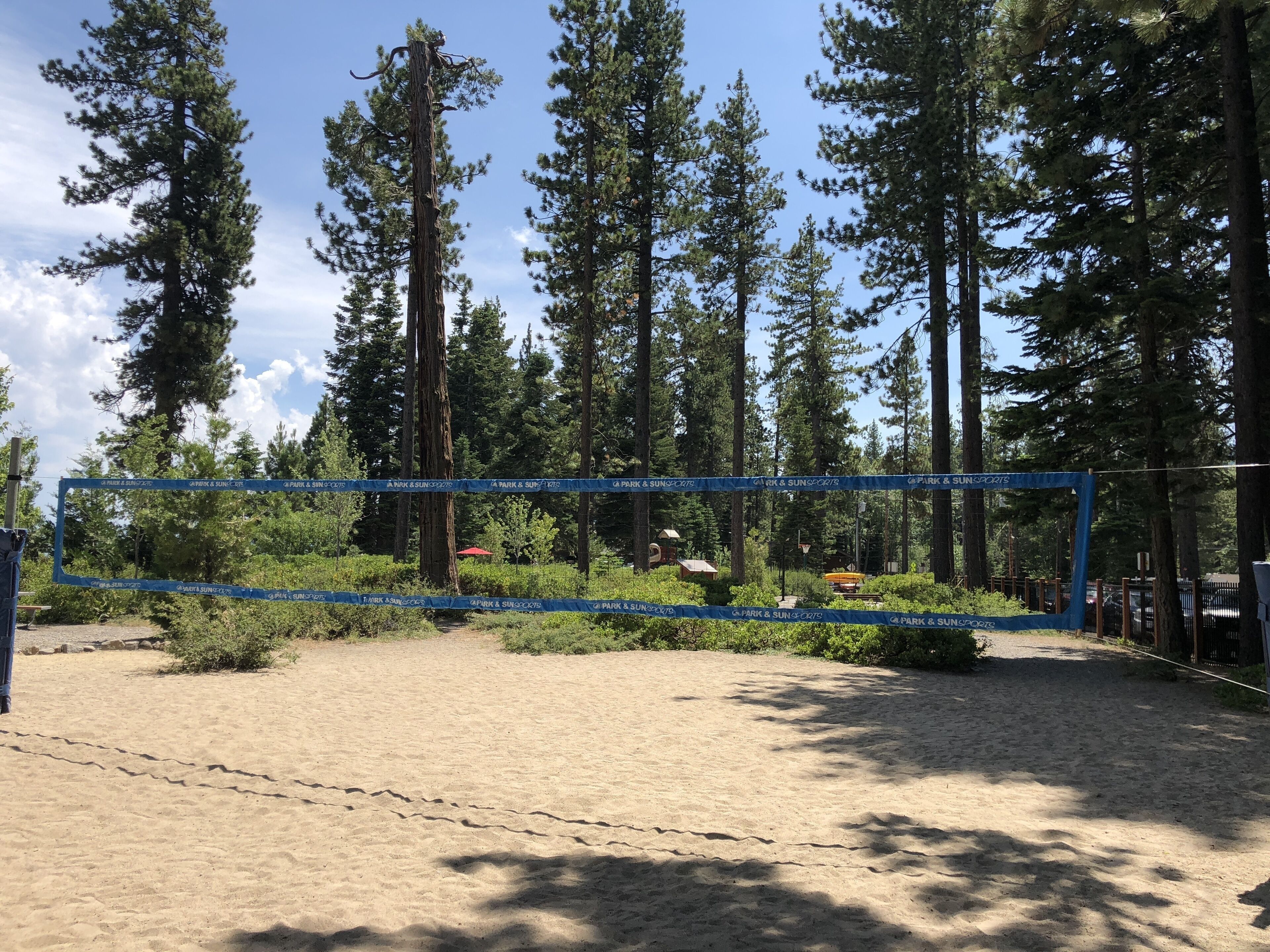 Une zone sablonne délimitée par une barrière faite d’une corde bleue, entourée de grands arbres et surplombée par un ciel dégagé.