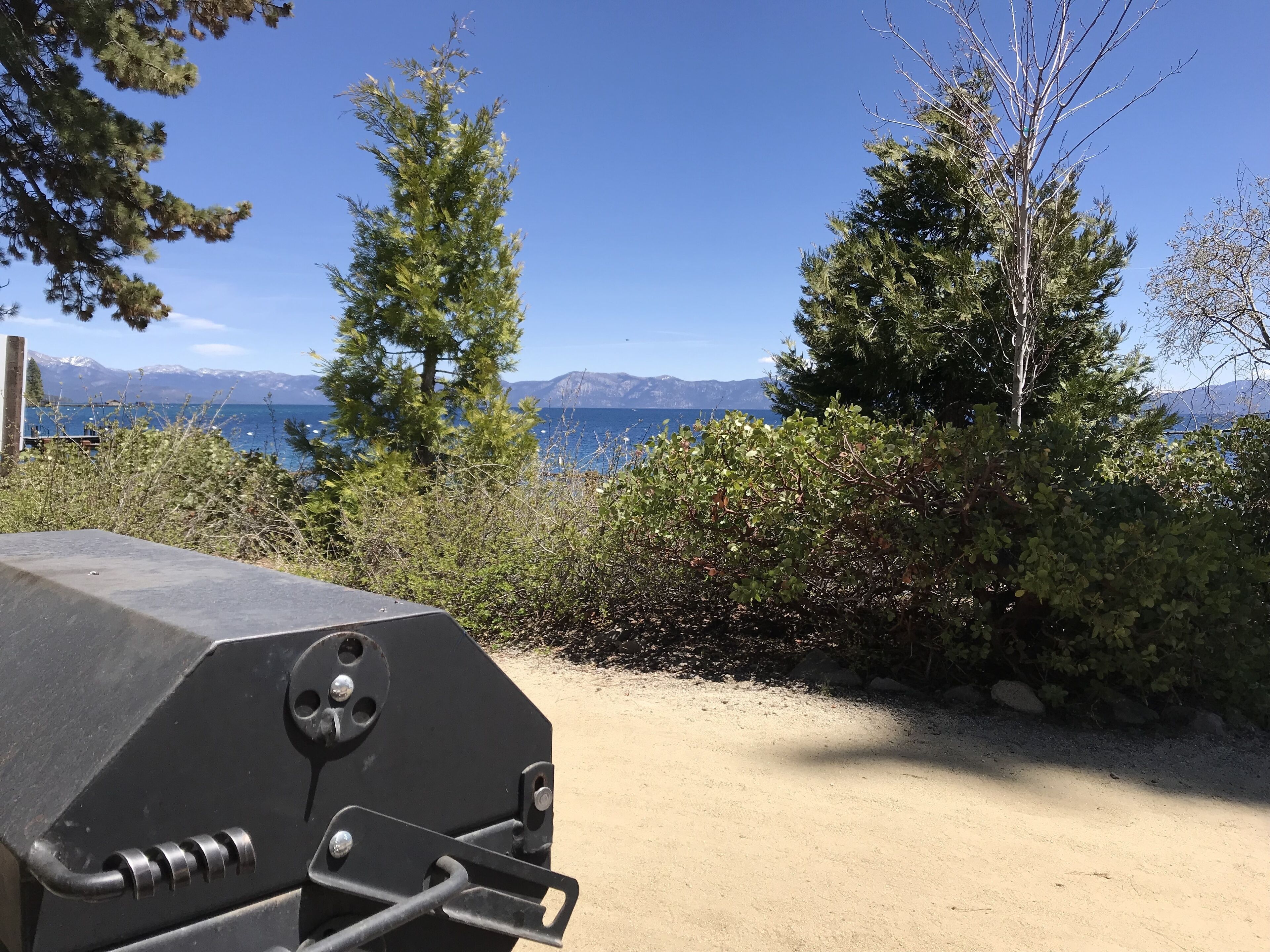 A barbecue grill in a natural setting with a view of mountains and a lake.