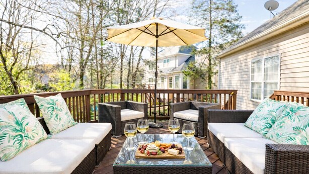 En udendørs terrasse med fletmøbler, et glasbord med mad og drikke samt en stor parasol.