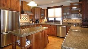 Una cocina con armarios de madera, encimeras de granito, electrodomésticos de acero inoxidable y una ventana con persianas.