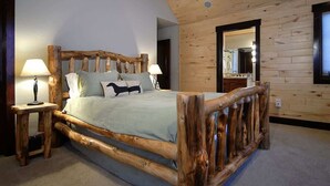 Una cama con estructura de madera, dos mesitas de noche, un espejo y una alfombra de color claro.
