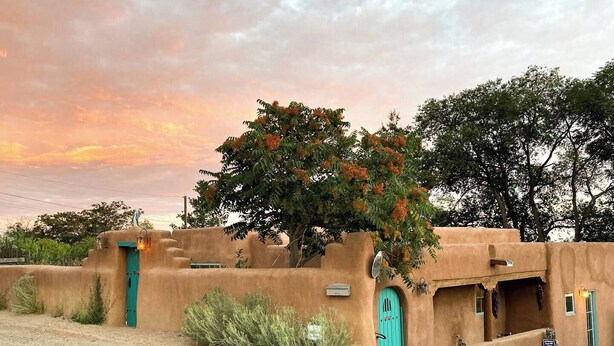 Un edificio tradicional de adobe con una puerta turquesa y una pequeña estructura adosada.