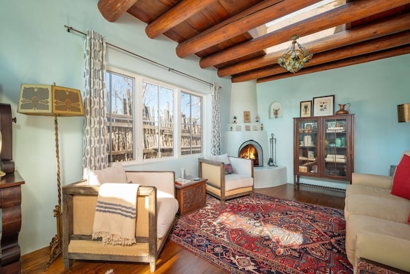 A cozy living room with a fireplace, wooden beams, and a large rug.