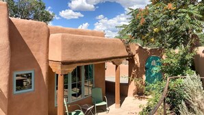 Un edificio tradicional de adobe con un patio cubierto, una puerta verde y una pequeña ventana con un cuadro enmarcado.
