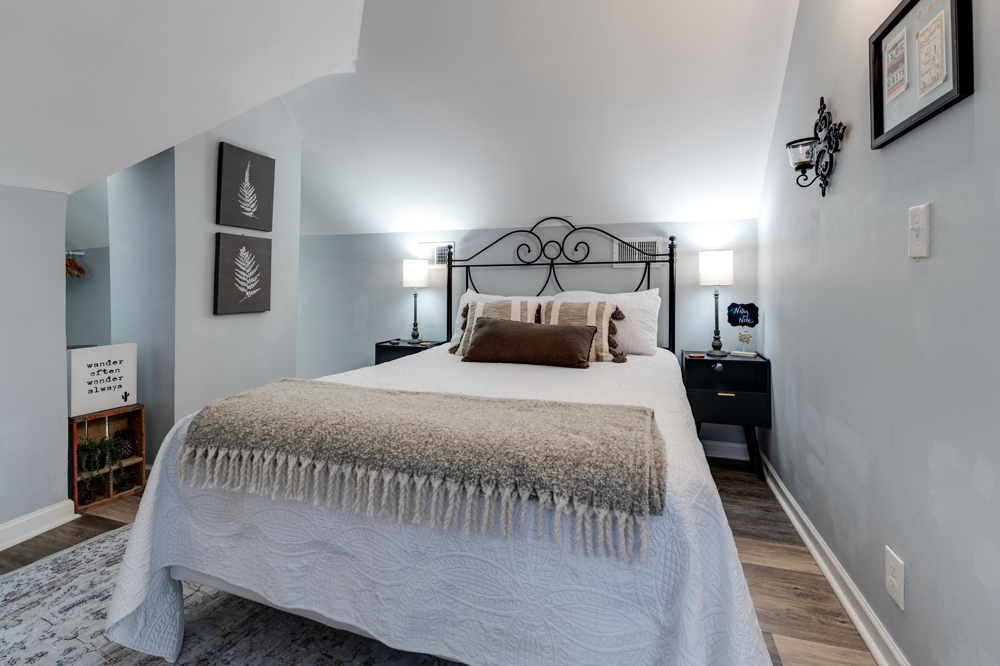 A bedroom with a bed, two bedside tables, wall-mounted lamps, and framed artwork.