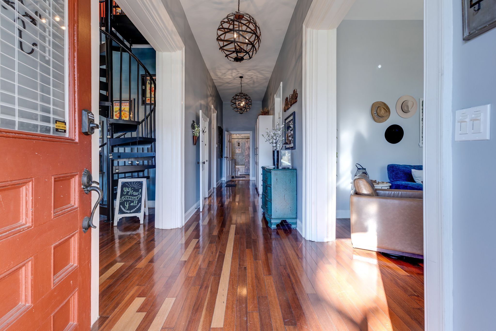 A hallway with a wooden floor, a red door, a staircase, and a blue sofa.