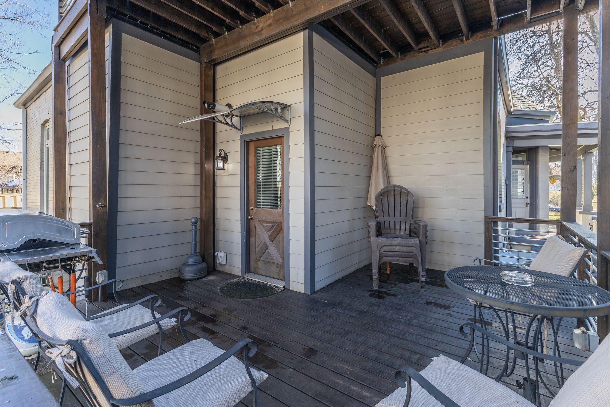 Eine überdachte Veranda mit Grill, Sitzgelegenheit im Freien und einer Tür mit Fenster.