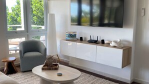 Ein modernes Wohnzimmer mit einem großen Flachbildfernseher an der Wand, einem grauen Sofa, einem runden Couchtisch und einem weißen Konsolentisch mit Dekoration.