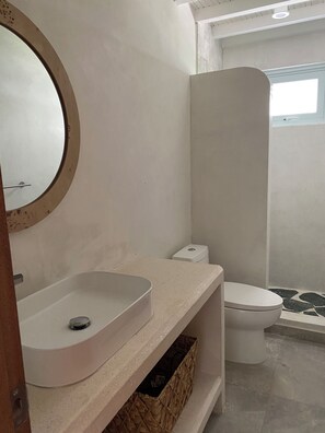 Ein Badezimmer mit rundem Spiegel, Waschbecken in Weiß, Toilette und Duschbereich.