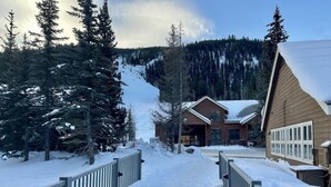 A snow-covered pathway leading to a lodge with a wooden exterior and a mountain backdrop. - Slopeside Beautifully Renovated Kitchen & Bath 1.5 Baths Deck Outstanding Views (Keystone)